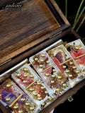 These handcrafted dominoes by Jadeari Handmade, titled "Antique Fairies," come in a rich wooden box. Each piece is a miniature work of art, with a pearlescent background and a clear resin top. Inside, they hold delicate, glittery gold flakes, tiny pebbles & bronze shimmer, and enchanting vintage illustrations of fairies in whimsical poses. The dominoes are marked with metallic chrome gold dots or pips.